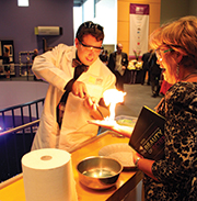 The SCI's outreach presenter  Kyle Schura (safely!) lights a  guest's hand on fire.