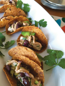 Mini tacos start with sweet pepper and flax seed shells dried in a dehydrator, which are then filled with black beans, avocado, salsa, almond herb cheese, and cashew cream seasoned with chipotle in adobo. 