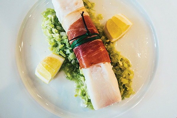 The baked halibut is wrapped in La Quercia prosciutto and served atop a bed of sautéed leeks. 